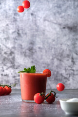 tomato juice in a glass, fresh tomato juice, cherry tomatoes and juice, parsley and salt, on a gray background