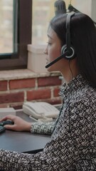 Wall Mural - Vertical video: Close up of asian woman with headphones talking on phone call to people at customer service. Consultant using headset and microphone, working at call center on computer. Support chat