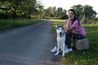 © Diana - A young woman sits with her husky dog on the side of a village road and waits for a car for hitch-hiking