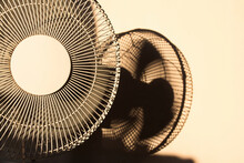 An Electric Fan With Blurred Blades Moving Casting A Blurry Shadow On The Plain White Wall In The Background