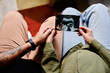 © Seventyfour - Close up of tattooed gay couple with pregnant young woman looking at ultrasound image of baby, same sex family