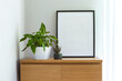 Mock up black frame with a houseplants on a shelf. White shelf against a white wall. Copy space
