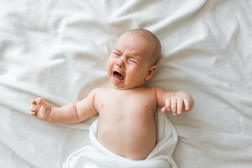 Wall Mural - Newborn baby cries on a white sheet. Childish tantrums. Colic and abdominal pain in infants. Medicines and vitamins for babies. Top view