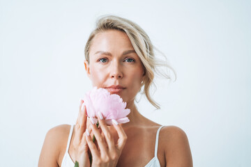 Beauty portrait of blonde hair smiling young woman with pink peony in hand isolated on white background