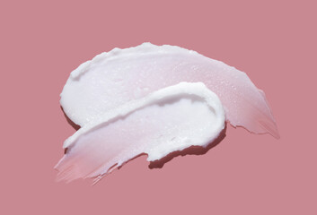 White cosmetic cream lotion swatch smear smudge on pink color background.