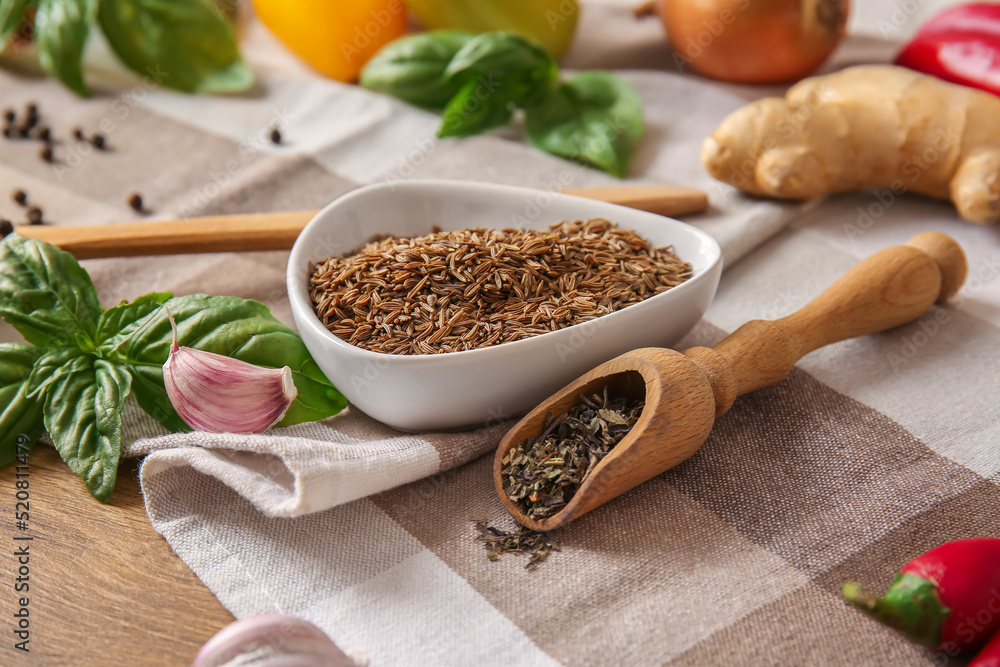 Bowl of cumin seeds and scoop with dried herbs on table