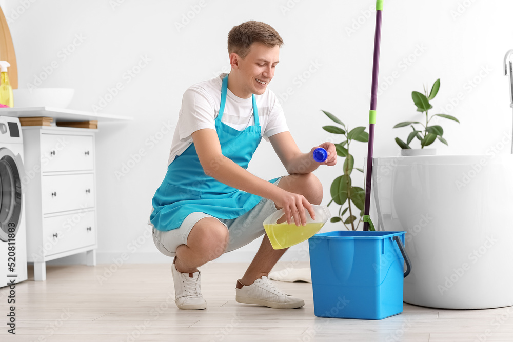Young man pouring detergent into bucket in bathroom