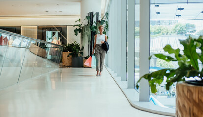 Happy businesswoman holding paper bags and walking in the modern shopping mall with big windows