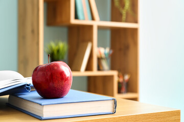 Wall Mural - Red apple with school books on desk in classroom, closeup