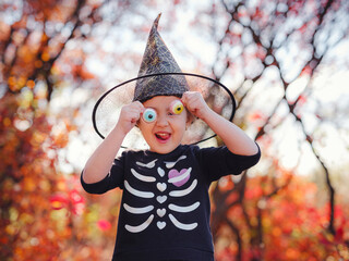 Young girl in black costume goes trick or treating. Little witch, Kids with jack-o-lantern. Children with candy bucket in fall forest. Happy Halloween.