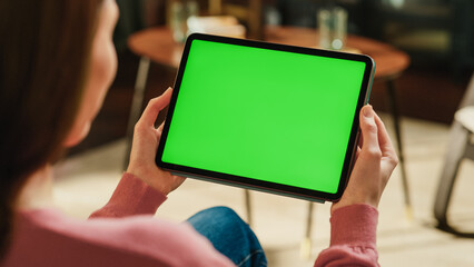 Fototapete - Female Holding Tablet Computer with Green Screen Mock Up Display. Woman Relaxing at Home, Watching Videos and Reading Social Media Posts on Mobile Device. Close Up Over the Shoulder Photo.