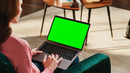 Fototapete - Young Adult Woman Working from Home Loft Apartment on Laptop Computer with Green Screen Mock Up Display. Creative Female Browsing the Web, Writing on Social Media. Close Up Over the Shoulder Photo.