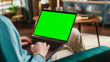 Aufkleber - Young Adult Man Working from Home Loft Apartment on Laptop Computer with Green Screen Mock Up Display. Creative Male Browsing the Web, Writing on Social Media. Close Up Over the Shoulder Photo.