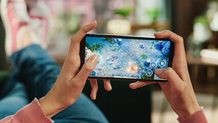 Aufkleber - Female is Relaxing on a Couch at Home, Playing an Interactive PvP RPG Strategy Video Game on Her Smartphone. Gamer Lies on a Sofa in Living Room. Close Up POV Photo of Mobile Device Screen.