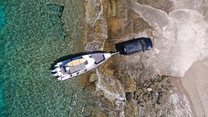 Aerial top view photo of speed boat on transport trailer being towed by truck from emerald sea shore to land