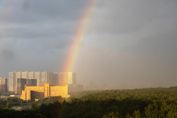 Wall Mural - rainbow over high-rise building and city park in rain before thunderstorm on sunny summer day