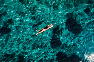 Wall Mural - Surf girl on surfboard in transparent ocean. Aerial view of surfer
