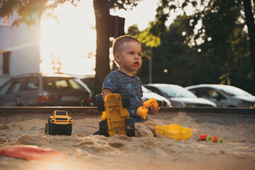 Wall Mural - Kid playing with toys in sandbox. Little boy having fun on playground in sandpit. Outdoor creative activities for kids. Summer and childhood concept