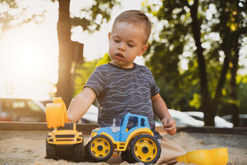 Wall Mural - Child playing with toys in sandbox. Little boy having fun on playground in sandpit. Outdoor creative activities for kids. Summer and childhood concept