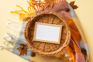 Wall Mural - Autumn inspiration concept. Top view photo of wicker basket with wooden photo frame anise yellow maple leaves pine cones and plaid on isolated pastel beige background with blank space