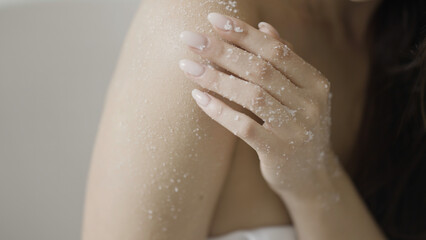 Bodycare concept, sensual woman applying scrub on her body. Action. Sugar scrubbing of her shoulder and arm.