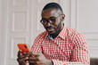 © VK Studio - Cheerful millennial biracial man using smartphone, sitting at desk