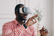 © VK Studio - Young african businessman wearing VR glasses touching 3d objects, interacting with virtual reality