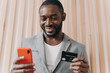 © VK Studio - Happy african businessman in suit holding credit card and mobile phone while doing online shopping