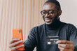 © VK Studio - Smiling African American businessman using credit card and smartphone while sitting at workplace