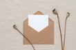 © Yulia - Blank white card mockup in brown envelope with poppy boxes, beige linen textile background. Top view, flat lay.