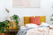 © brizmaker - Bed with crumpled plaid, cushions, side table and houseplants