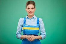 Smiling Woman In Blue Overalls Standing With Folded Hands. Isolated On Green Background.