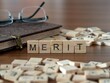 merit word or concept represented by wooden letter tiles on a wooden table with glasses and a book