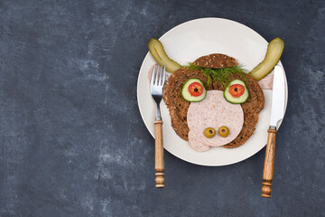 Sandwich in the form of a cheerful bull made of bread,s ausages and vegetables