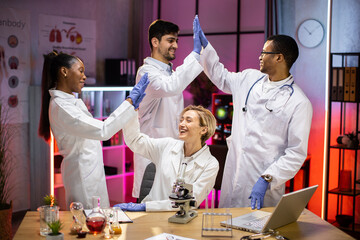 Wall Mural - Professional international medical scientists giving high five after ending of the experiment in modern biology laboratory.