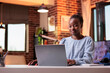 © DC Studio - Female african american remote student typing on laptop in room with modern interior. Smiling freelance copywriter using portable computer in home office with beautiful warm sunset light
