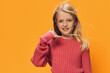 a beautiful, sweet girl in bright, pink clothes, stands on a yellow background with her fingers folded in the form of a phone. Horizontal studio photo with empty space to insert advertising layout