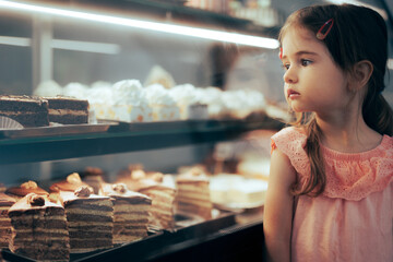 Little Girl Checking Desserts in a Showcase Window of a Confectionery Shop. Toddler child deciding which cake to eat in a baker shop
