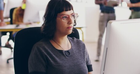 Sticker - A serious and young woman designer sitting and working on a computer at the office with colleagues in the background. Female manager typing on a desktop while focused at the screen.