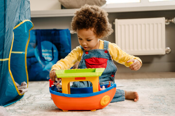 Little cute african curly boy playing with toyship at home