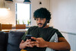 © Drobot Dean - Young indian handsome calm man sitting on sofa with phone