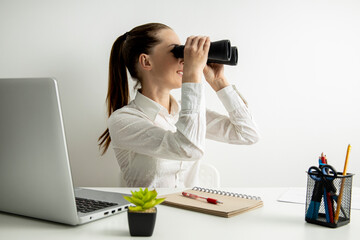 Wall Mural - Young woman sitting in the office at the workplace looking through binoculars