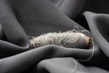 A Reel With Gray Threads In A Draped Soft Fabric, Close-up, Macro. Atelier, Tailoring, Sewing Background. The Texture Of Silk Threads And Satin Fabric. Fashion Designer, High Fashion Concept