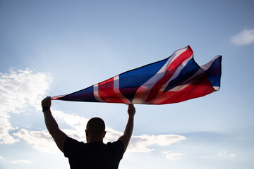 Wall Mural - Man holding British flag against blue sky