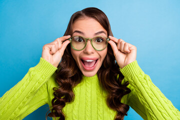 Poster - Photo of astonished cute pretty girl with curly hair wear green sweater impressed holding glasses isolated on blue color background