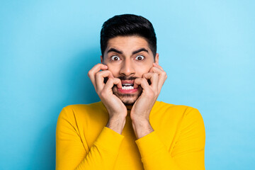 Photo of shocked scared man wear yellow sweater biting fingers isolated blue color background