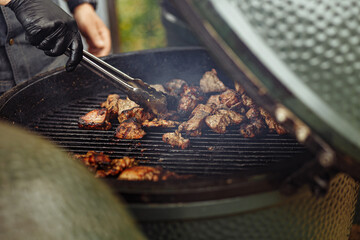 Close up image of The Green Egg outdoor barbecue. Very popular ceramic bbq. A hand of a cook preparing BBQ