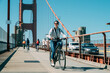© PR Image Factory - full length asian woman is enjoying cityscape while cycling at leisure on golden gate bridge in San Francisco California on a sunny day with vehicles passing by