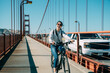 © PR Image Factory - happy Asian girl is laughing at the camera while having fun riding a bicycle at summer time on golden gate bridge with cars passing by in San Francisco USA