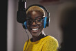 canvas print picture - Optimistic ethnic female radio host in bright yellow sweater headphones and glasses recording podcast near microphone in studio